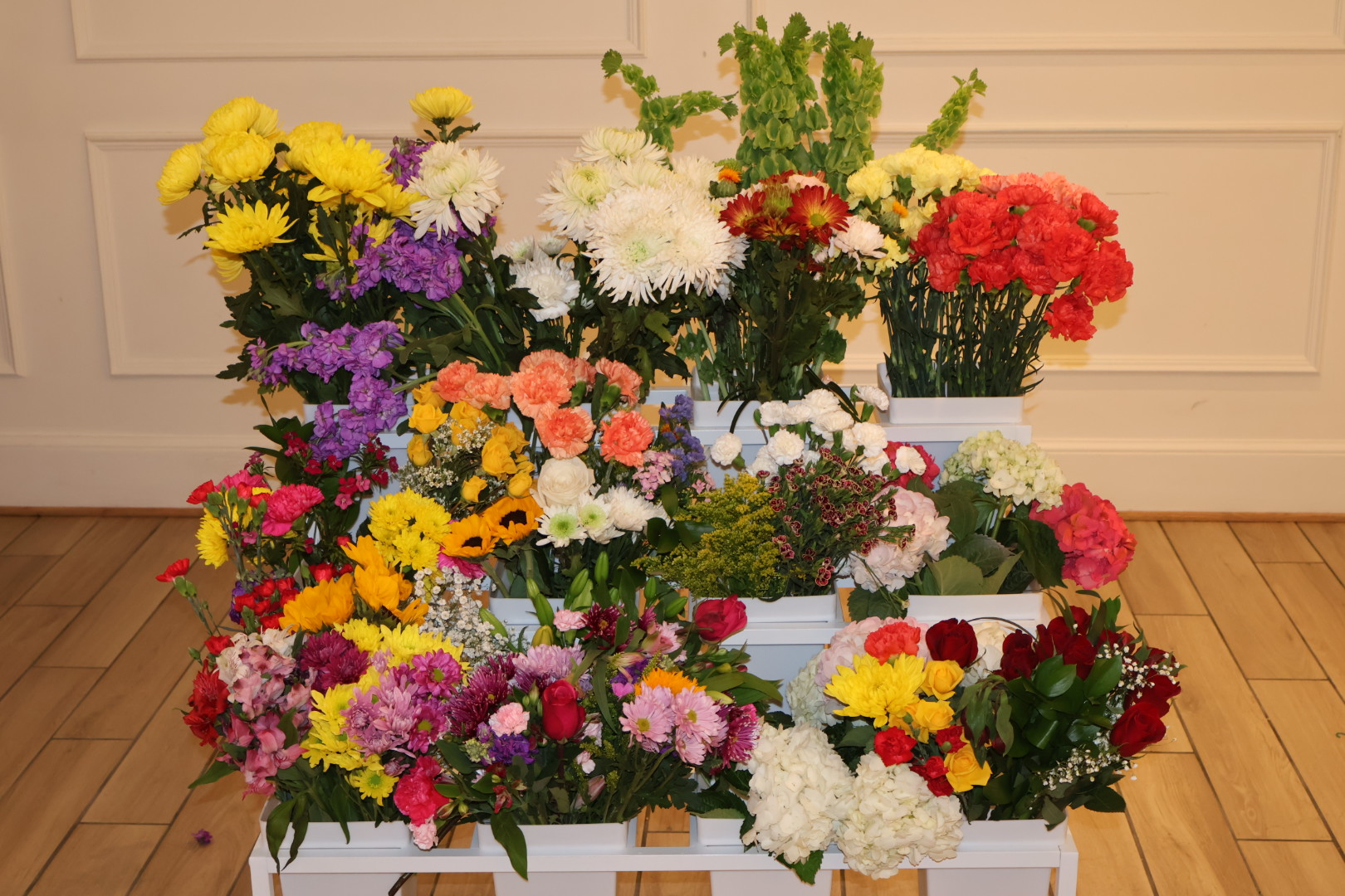 A colorful display of fresh flowers in white crates, including yellow, pink, purple, red, and white blooms